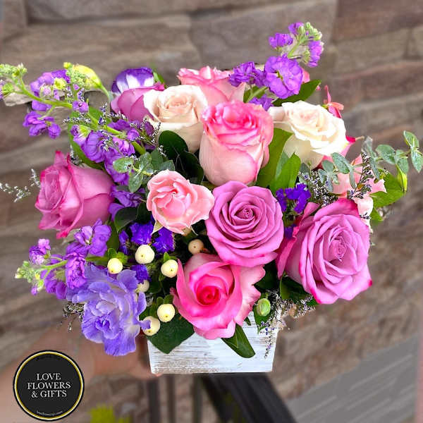 Pink and lavender roses with purple accent flowers in a whitewashed wooden box