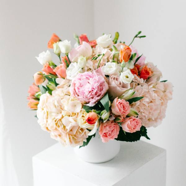Mixed bouquet of pink, peach, and white flowers in a white vase