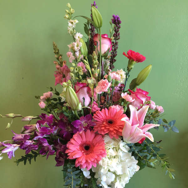 Tall mixed bouquet with pink lilies, gerbera daisies, orchids, and white hydrangea in a glass vase