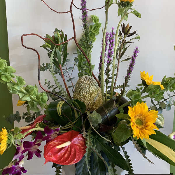Tall floral arrangement with sunflowers, orchids, and a red anthurium