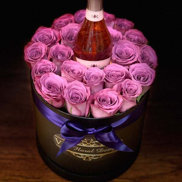 Pink roses arranged around a champagne bottle in a round box