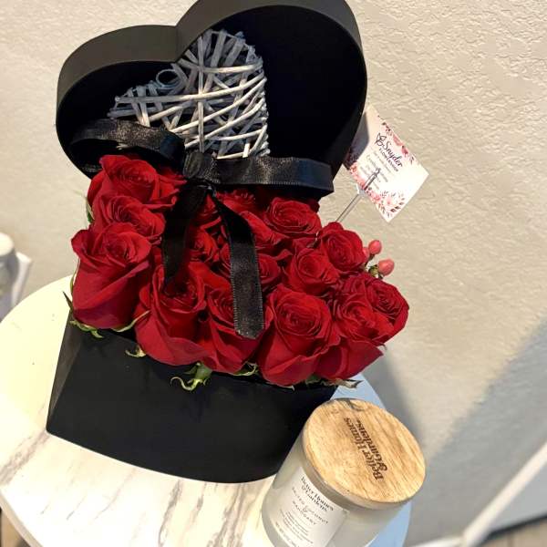 Red roses arranged in a black heart-shaped box with a ribbon and wicker heart topper