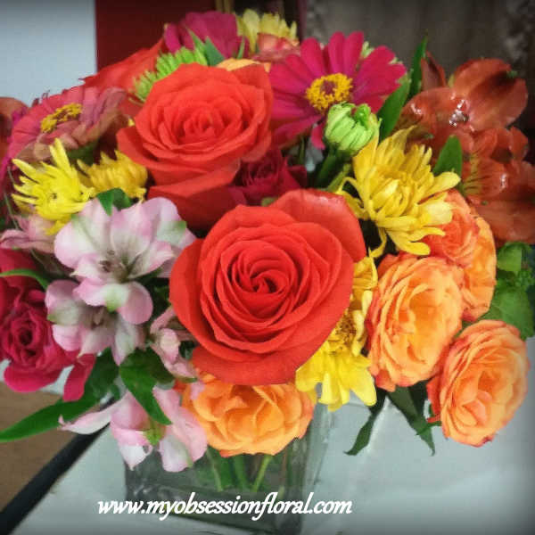Mixed bouquet of roses, daisies, and orange blooms in a glass vase