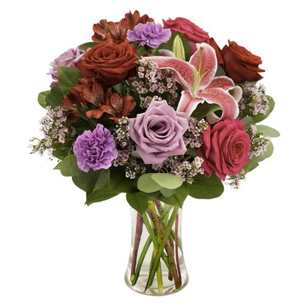 Mixed bouquet of roses, lilies, and carnations in a clear glass vase