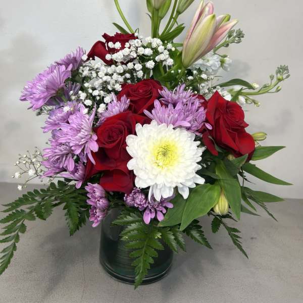 Bouquet of red roses, pink lilies, and purple chrysanthemums in a glass vase