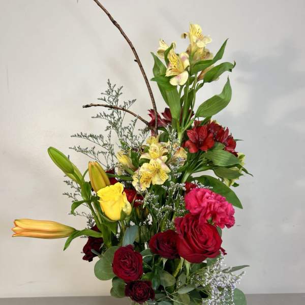 Tall bouquet of red roses, yellow lilies, and red alstroemeria in a glass vase