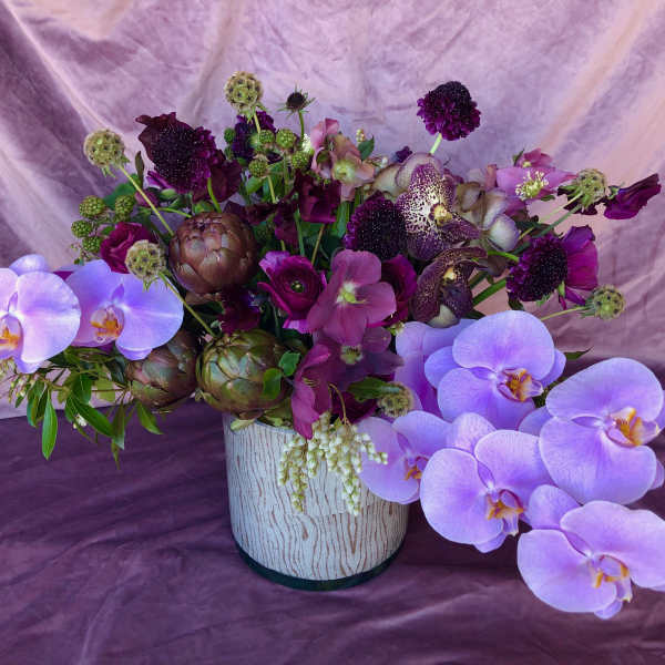 Purple floral arrangement with orchids in a white vase