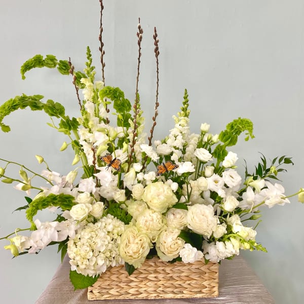 White floral arrangement in a woven basket with tall green accents