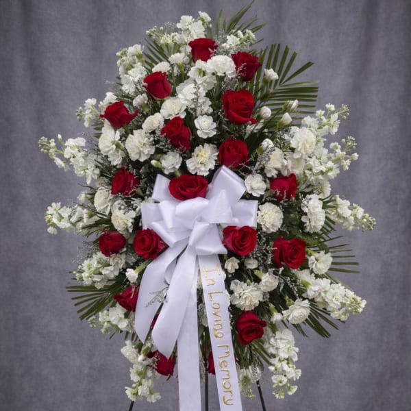 Standing red and white rose funeral spray with a white ribbon on an easel