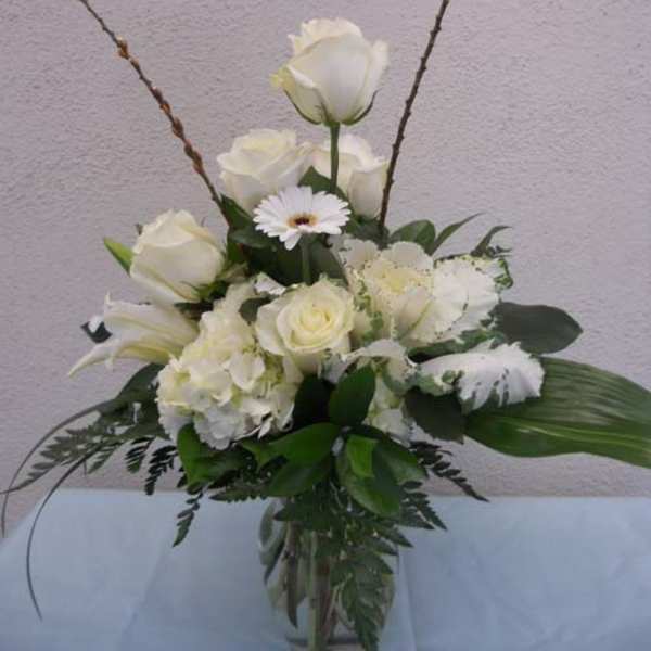 White roses and lilies arranged in a glass vase with a daisy accent