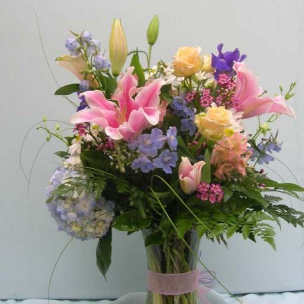 Mixed bouquet of pink lilies, roses, and blue flowers in a glass vase