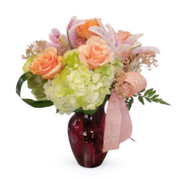 Bouquet of peach roses and hydrangeas in a red glass vase with a pink ribbon