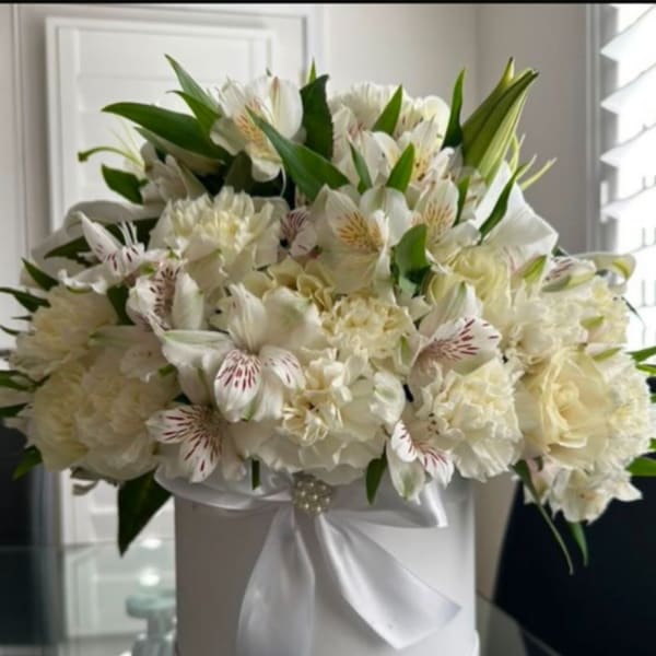 White floral arrangement in a round hat box with a satin ribbon