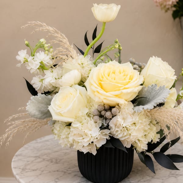 Cream roses and white flowers in a black vase with dried grasses