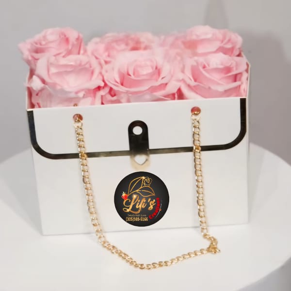 Pink roses arranged in a white gift box with a gold chain strap.