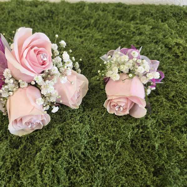 Two small pink rose corsages with white baby's breath and ribbon