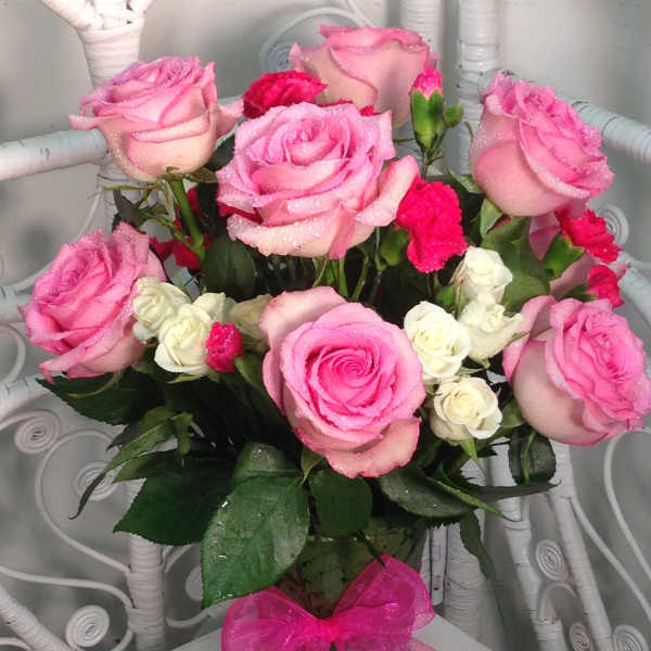 Pink and white roses arranged in a glass vase with a pink bow.