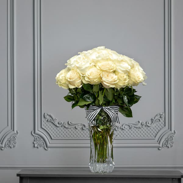 Cream rose bouquet in a clear glass vase with a striped ribbon