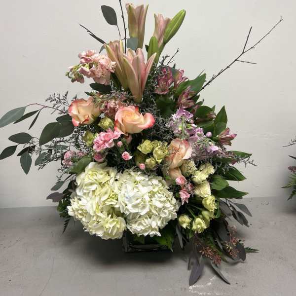 Tall floral arrangement with lilies, roses, hydrangeas, and mixed greenery