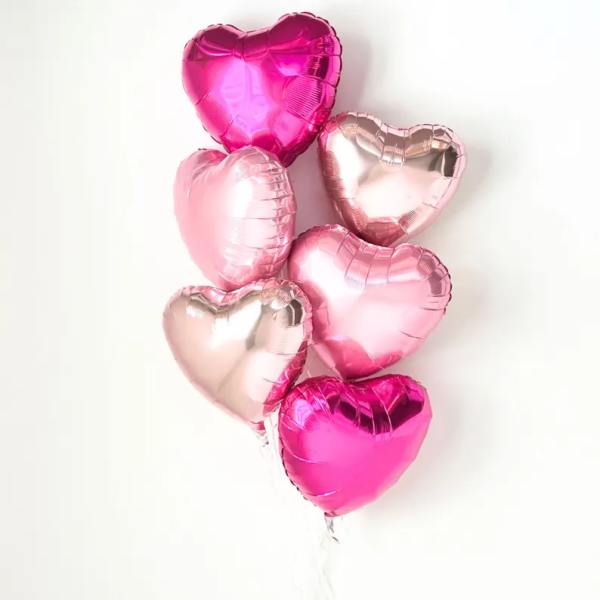 Cluster of heart-shaped pink and rose-gold balloons on a white background