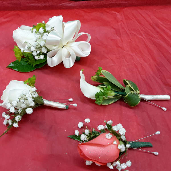 Four small boutonnieres and corsages on red fabric, with white and pink flowers.