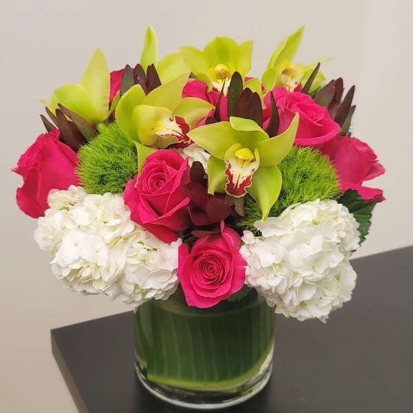 Pink roses and green orchids in a glass vase with white hydrangeas
