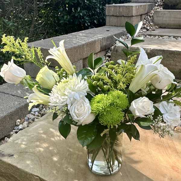 White flowers and green blooms arranged in a clear glass vase