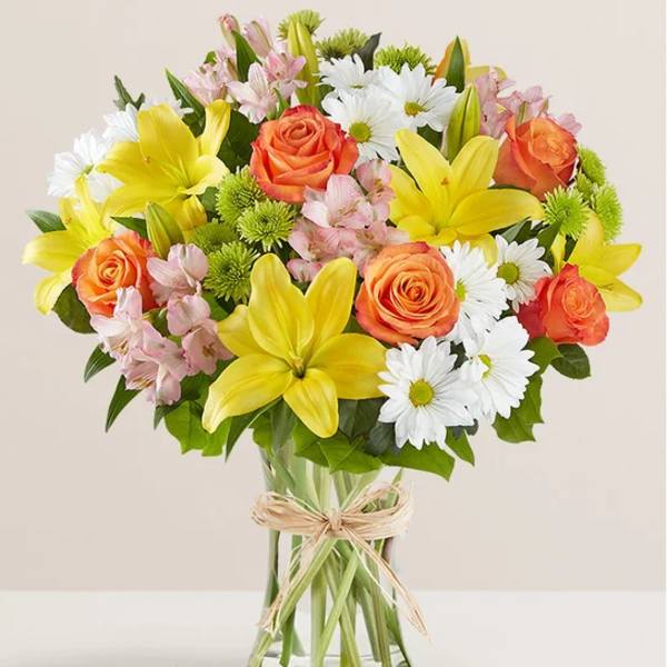 Bouquet of yellow lilies, orange roses, and white daisies in a glass vase