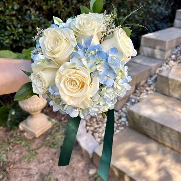 Handheld bouquet of white roses and pale blue hydrangeas with green ribbon