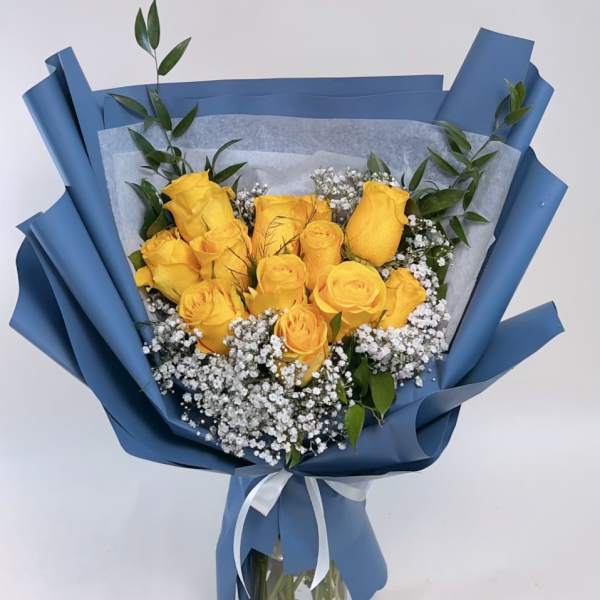 Yellow roses in blue wrapping with baby's breath in a glass vase