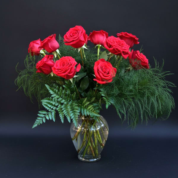 Red roses arranged in a clear glass vase with airy greenery
