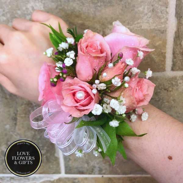 Pink rose wrist corsage with white filler flowers, pearls, and sheer ribbon on a wrist