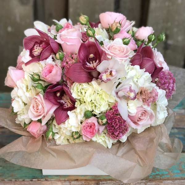 Pink and white bouquet with roses, orchids, and hydrangeas wrapped in paper