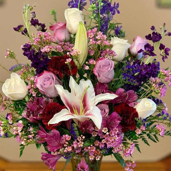 Mixed bouquet of lilies, roses, and purple flowers in a glass vase