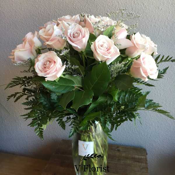 Tall vase arrangement of pale pink roses with white filler flowers.