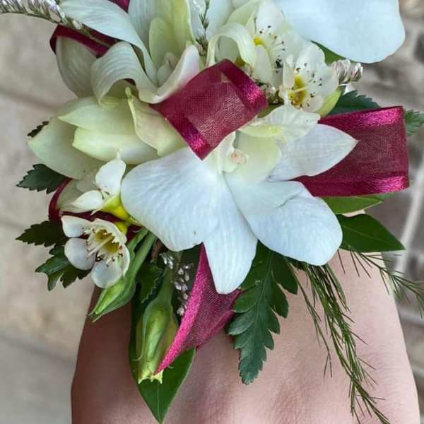 White floral wrist corsage with magenta ribbon accents
