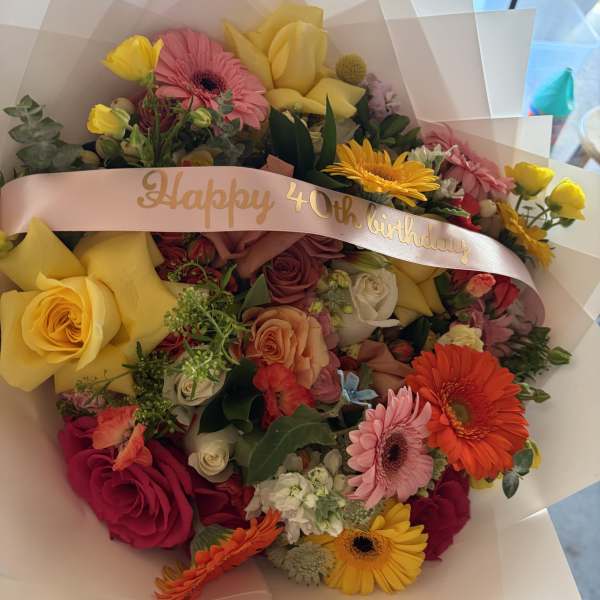 Mixed bouquet with roses, gerbera daisies, and yellow tulips, wrapped with a birthday ribbon