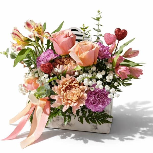 Mixed bouquet of pink and peach flowers in a marble box with heart picks