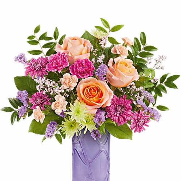 Peach roses and pink flowers in a purple glass vase