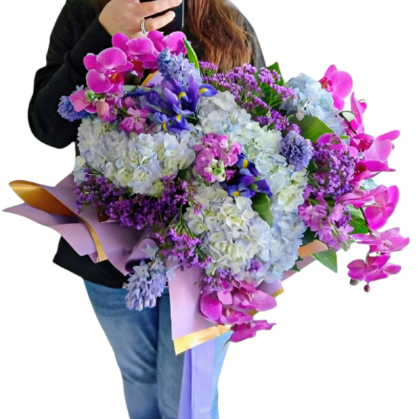 Large bouquet of pink orchids, blue hydrangeas, and purple flowers wrapped in pastel paper