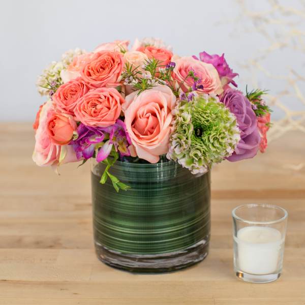 Pink and purple roses arranged in a glass vase beside a small candle