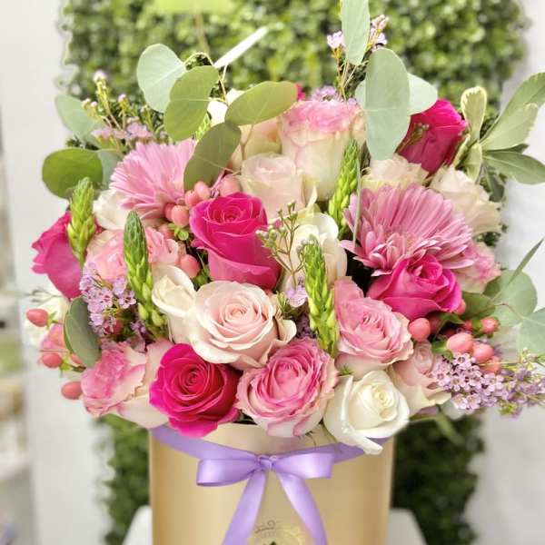 Pink and white roses with pink gerbera daisies arranged in a gold hatbox with a lavender ribbon
