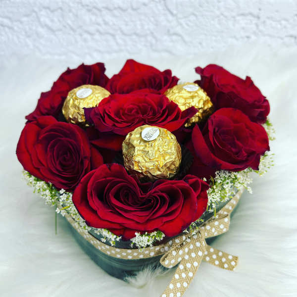 Red roses arranged with gold-wrapped chocolates in a round box