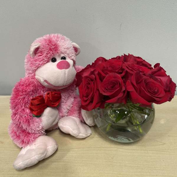 Pink teddy bear beside red roses in a glass bowl vase