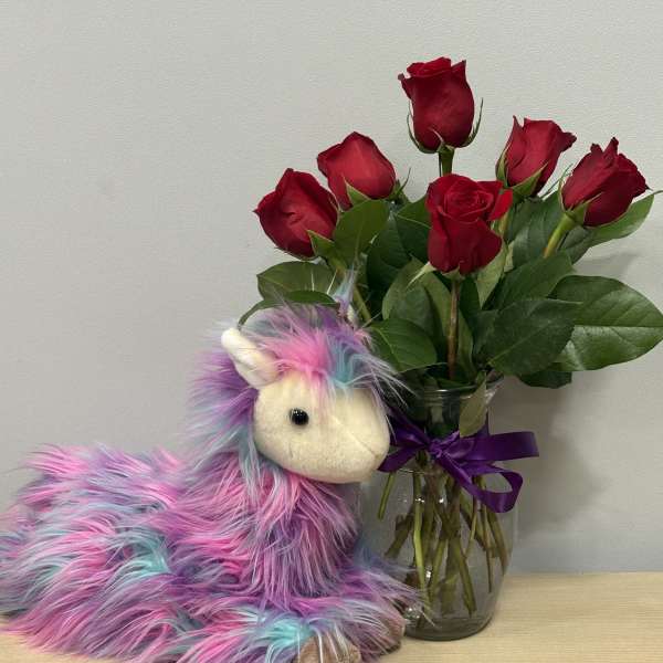 Red roses in a glass vase beside a colorful plush unicorn