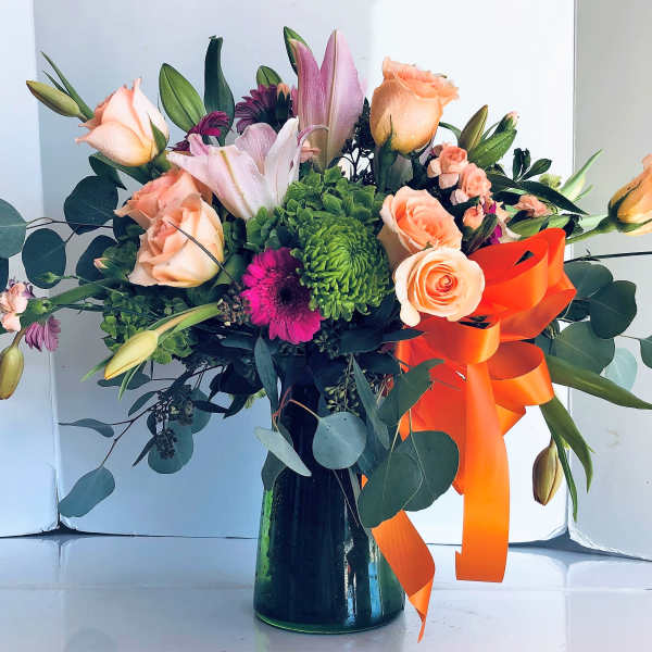 Mixed bouquet of peach roses, lilies, and green chrysanthemums in a dark vase