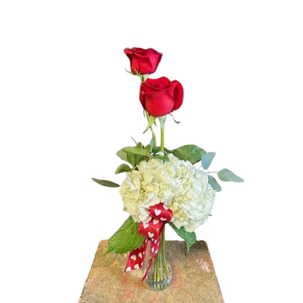 Two red roses above a white hydrangea bouquet in a glass vase