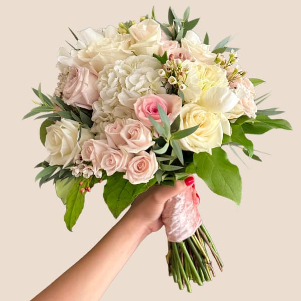 Handheld bouquet of pale roses and white hydrangeas with greenery
