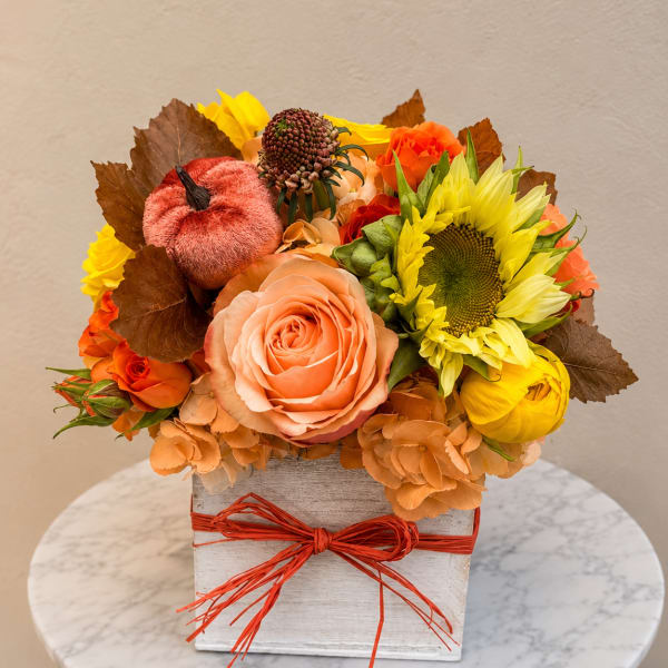 Autumn floral arrangement with roses and a sunflower in a square box