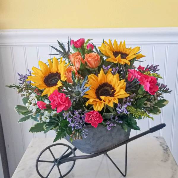Sunflowers, roses, and carnations arranged in a wheelbarrow planter